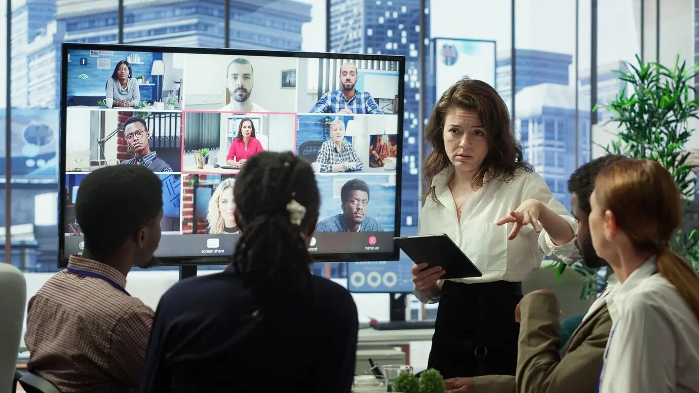 A business team in a boardroom attends a video call meeting with a group of investors to discuss.